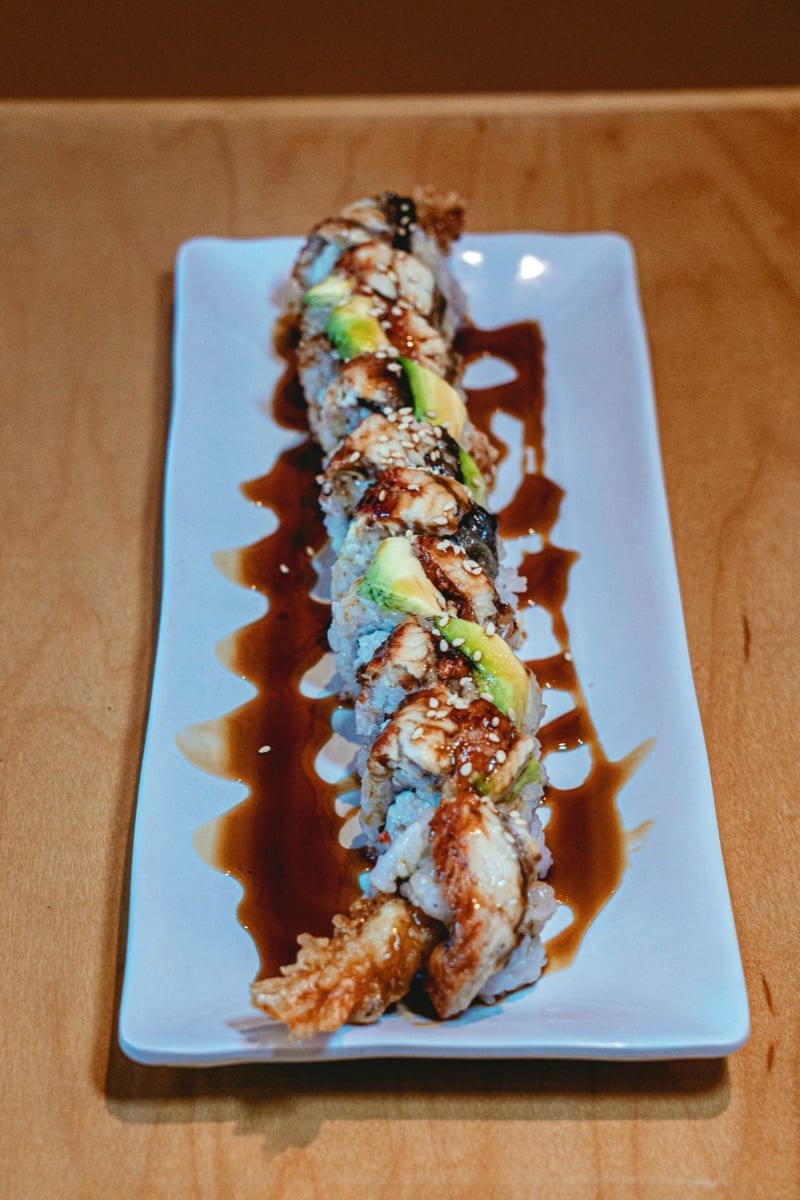 Sliced sushi roll topped with eel, avocado and sesame seeds on a white plate